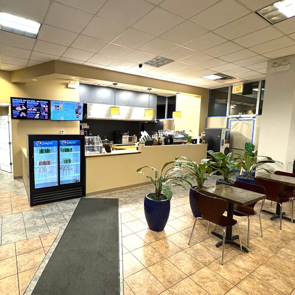 Interior view of a restaurant with a counter, menu screens, Pepsi coolers, and dining tables.
