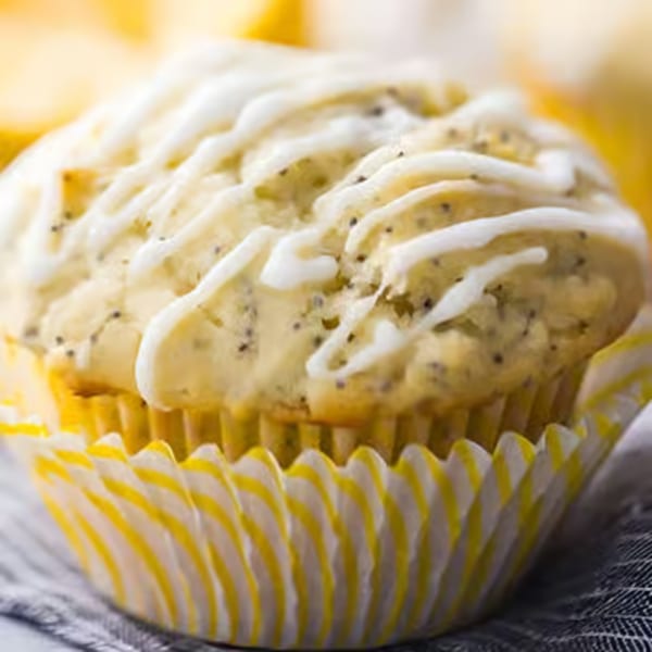 A lemon poppy seed muffin with white icing drizzle in a yellow and white striped wrapper.
