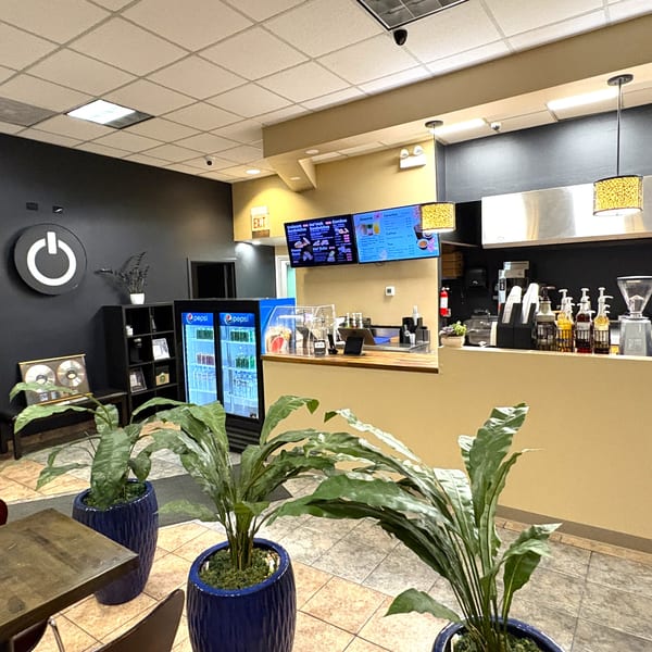 Interior view of a modern cafe with a counter, menu screens, and potted plants.