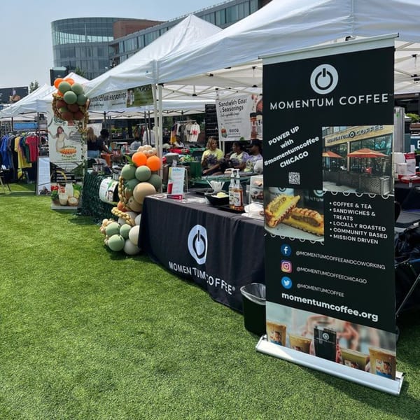 Momentum Coffee booth at an outdoor market with a large banner, table, and balloons on artificial grass.