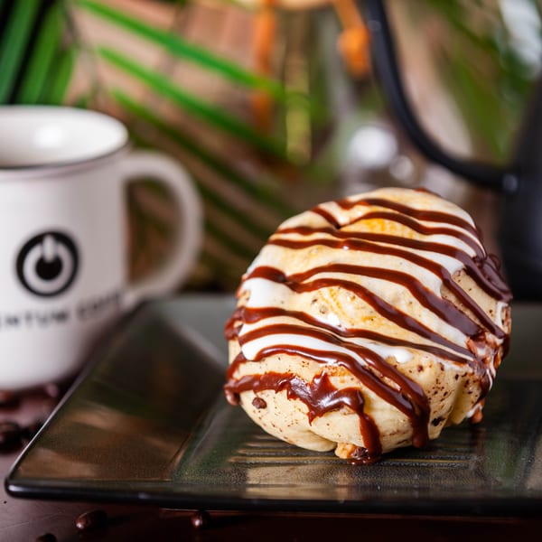 A Momentum Coffee cinnamon roll drizzled with chocolate and white icing, next to a branded mug.
