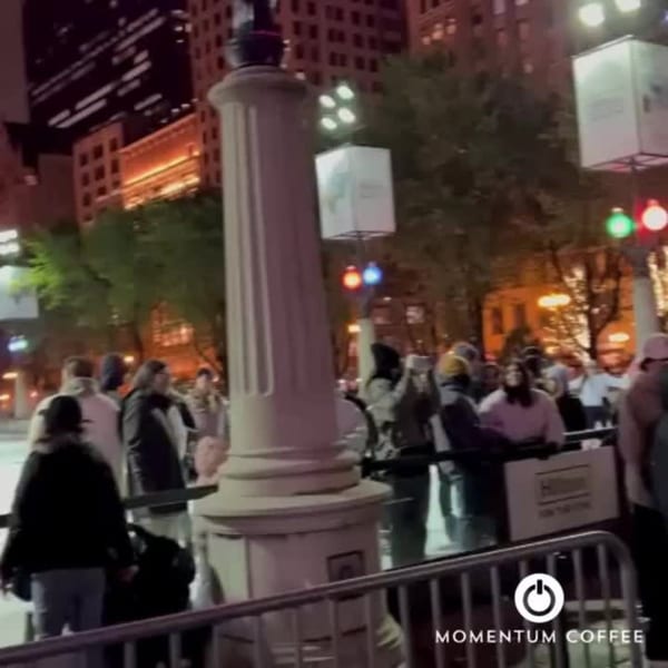 Momentum Coffee customers gathered outside at night, with city lights and a Hilton sign in the background.