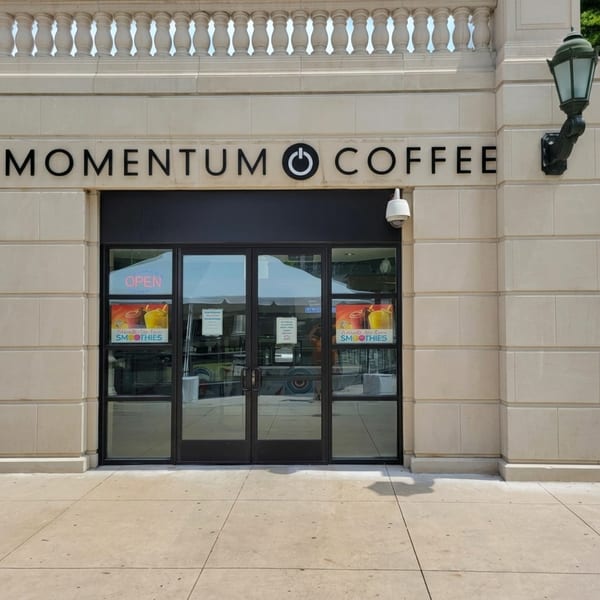 Momentum Coffee storefront with black lettering on a light stone building, an "OPEN" sign, and smoothie ads.