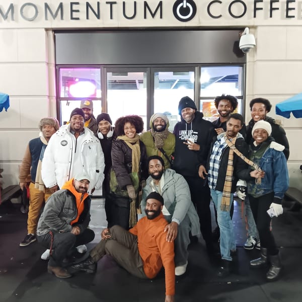 A large group of smiling people, some sitting and some standing, pose in front of Momentum Coffee.