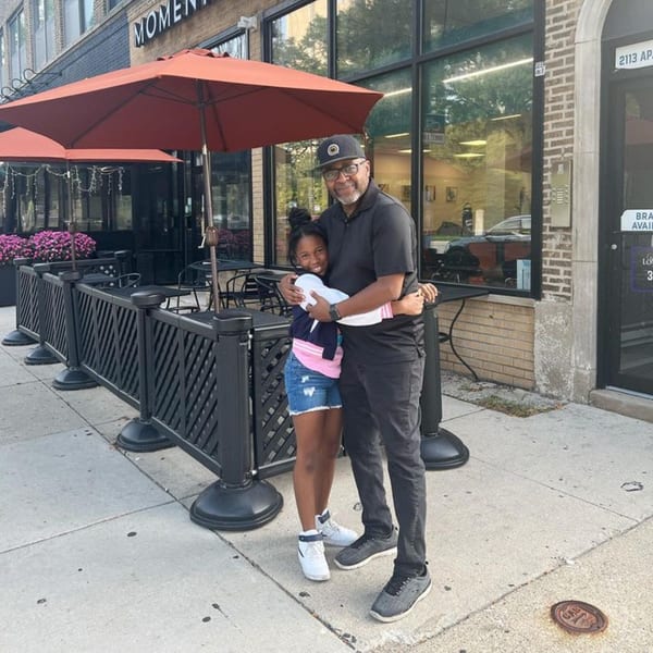 A man and a young girl hugging in front of Momentum Coffee's outdoor patio.