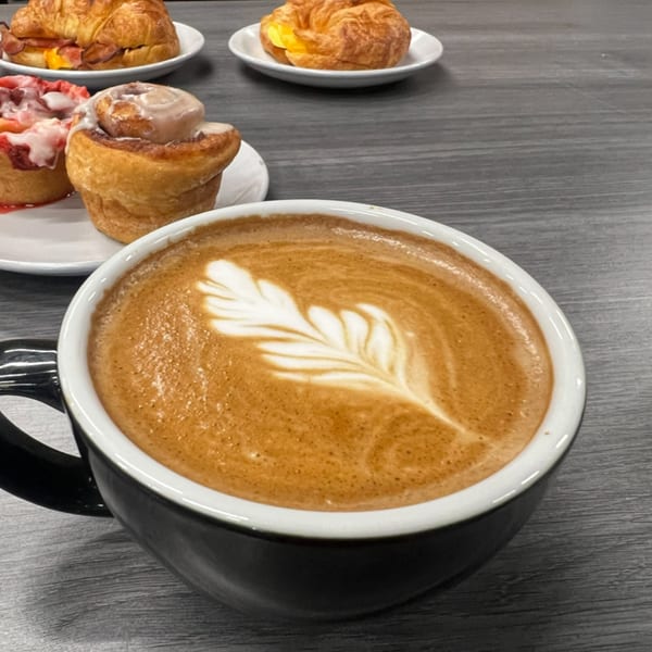 Momentum Coffee latte with leaf art, cinnamon rolls, and breakfast croissants on a gray table.