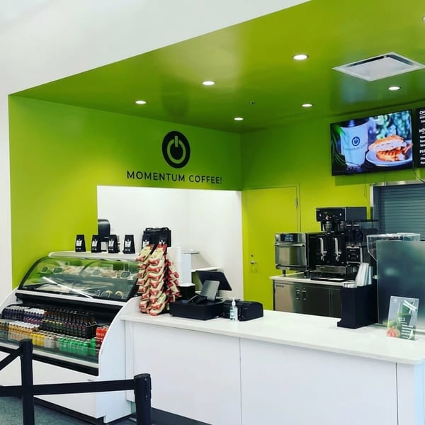 Momentum Coffee shop interior with bright green walls, a display case, and coffee machines.