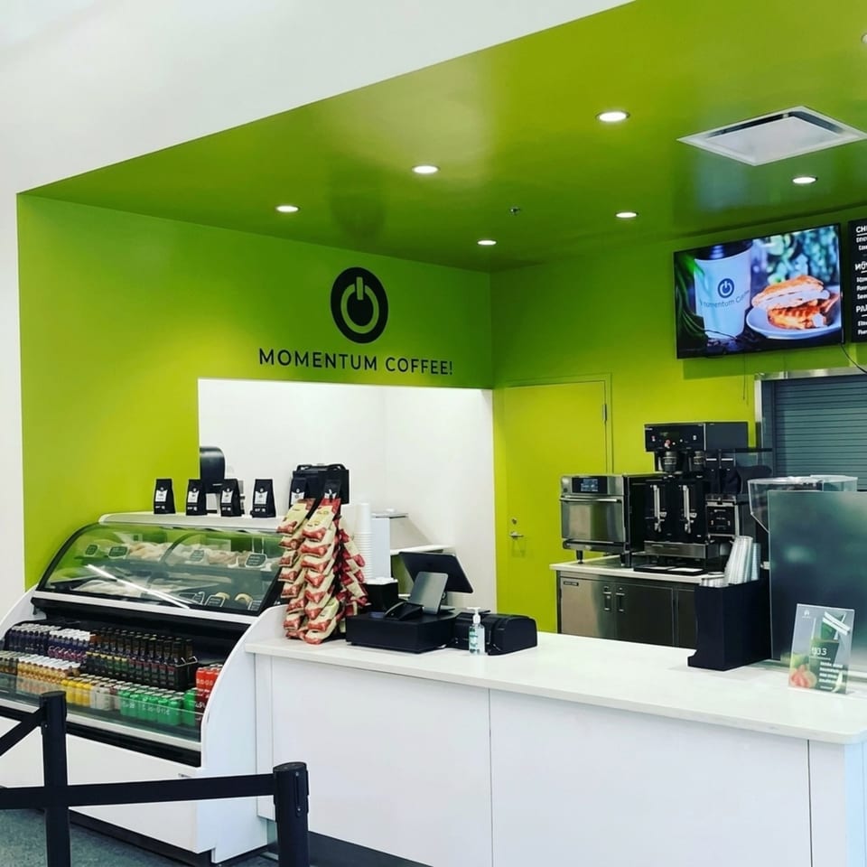 Momentum Coffee shop interior with bright green walls, a display case, and coffee machines.
